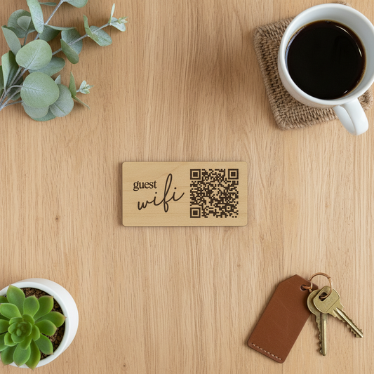 Wooden sign with 'guest wifi' and QR code on a wooden surface with a cup of coffee, keys, and plants.